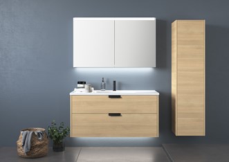Kaluste GRAND Solid 120, väri Nordic Oak, vetokahva MOOD, ja korkea kaappi 40 samaa sarjaa. Pesuallashana SLEEK. Peilikaappi STAGE 120.